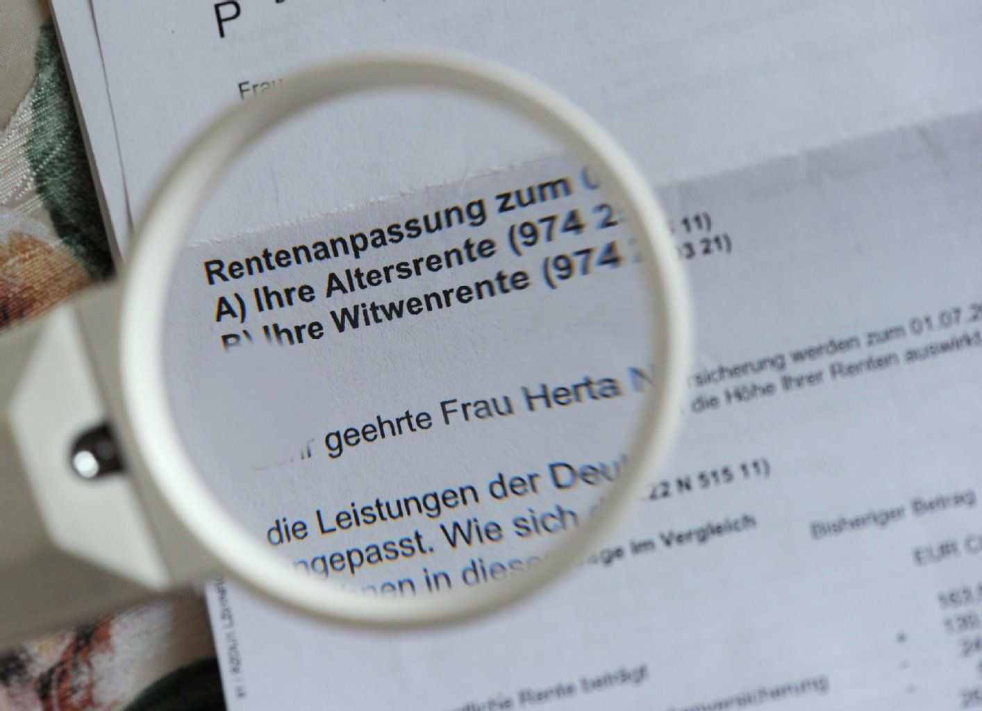 Ein Rentenbescheid wird mit einer Leselupe gelesen.