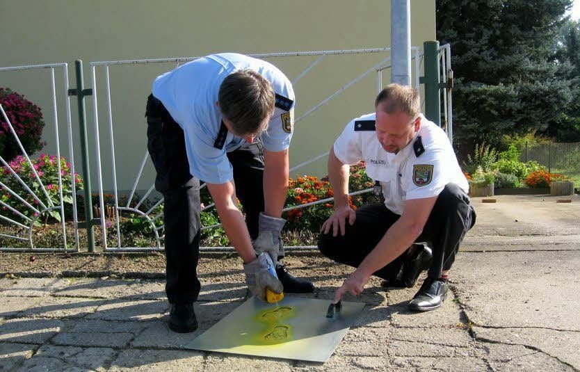 Michael Krebs (links) und Marco Kopitz sprühen vor der Gierslebener Grundschule gelbe Füße auf.