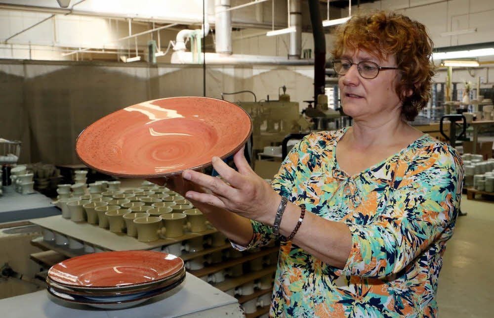 Heike Schäfer kontrolliert die Qualität eines Tellers an einem Sortier- und Schleifarbeitsplatz.