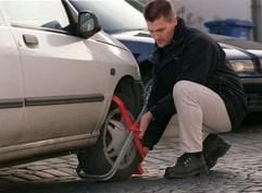 Das Archivbild zeigt einen Vollzugsbeamten, wie er eine so genannte Parkkralle an ein abgestelltes Auto montiert. Einige Bundesländer setzen Parkkrallen ein, um rückständige Kraftfahrzeugsteuer einzutreiben. (Foto: dpa)
