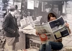Eine Besucherin der Ausstellung «Schwarz auf Weiß 400 Jahre Zeitung - ein Medium macht Geschichte» liest im Mainzer Gutenberg Museum vor einem Fotoposter, das einen Zeitungsstand zeigt, in einer Zeitung. (Foto: dpa)