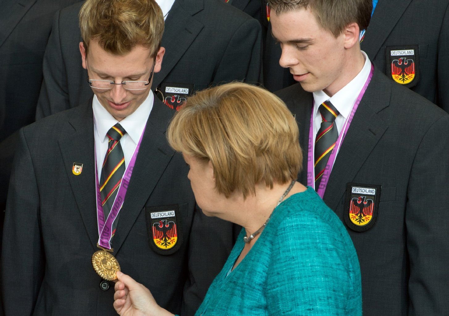 Bundeskanzlerin Angela Merkel (CDU) betrachtet im Kanzleramt in Berlin die Medaillen von Fliesenleger Björn Bohmfalk (l) und Stuckateur Andreas Schenk.
