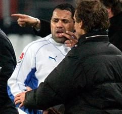 HSV-Spieler Ailton zeigt nach einem Zusammenstoß mit einem Gegenspieler seinem Trainer Thomas Doll seine Wange. Am Donnerstag wurde der Angreifer operiert. (Foto: dpa)