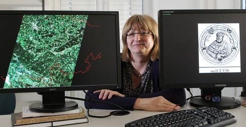 Christiane Schmullius, Professorin am Institut für Geographie, sitzt zwischen Monitoren, die ein Satellitenbild eines Waldgebietes (l.) und das Logo der Universität zeigen. (FOTO: DAPD)