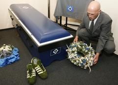 Bestatter Holger Langer richtet in Hamburg einen Kranz an einem blauen Sarg mit dem Logo des Hamburger SV. (Foto: dpa)