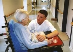 Ein Pfleger kümmert sich um eine Seniorin im Rollstuhl. (Archivfoto: dpa)