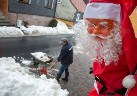 Eine Weihnachtsmannpuppe scheint einen Mann zu beobachten, der einen Schneehaufen vom Bürgersteig räumt. Das Tauwetter und die Wetterprognose lassen die Hoffnung auf weiße Weihnachten schwinden. (FOTO: DPA)