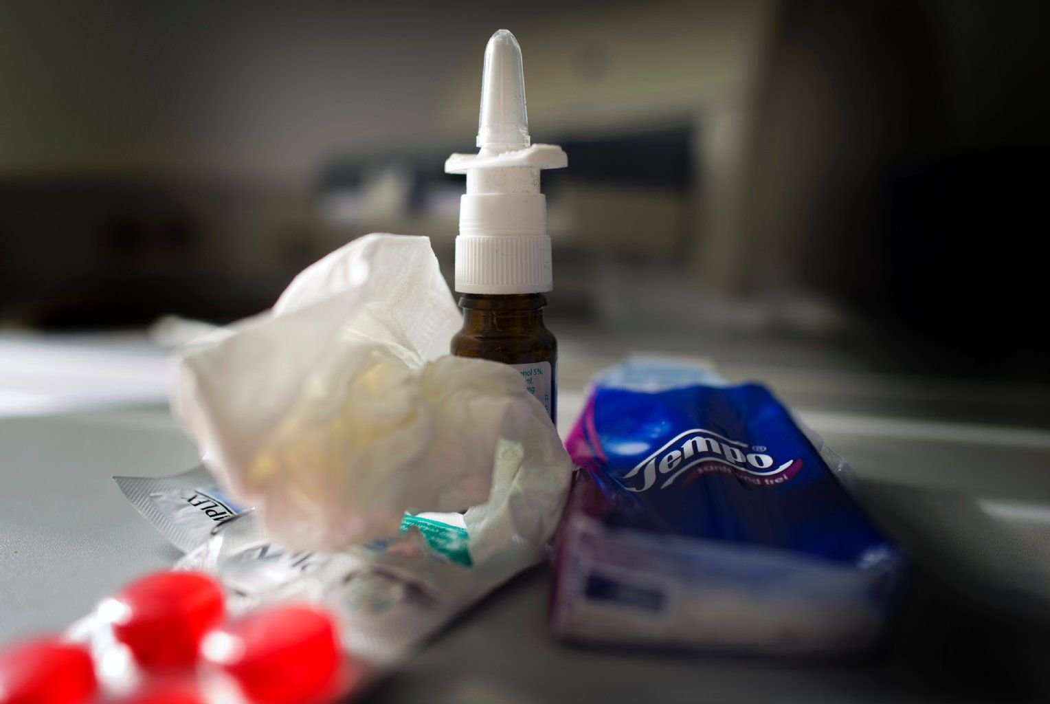 Anti-Erkältungsmittel wie Nasenspray, Halstabletten und Papiertaschentücher liegen auf einem Tisch