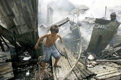 Ein junger Mann ist in den Trümmern der ausgebrannten Häuser des Slumviertels von Manila unterwegs, während Feuerwehrleute Glutnester löschen. (Foto: dpa)
