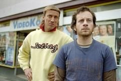 Im Kinofilm «Video Kings» stehen Flo (Fabian Busch, r.) und Hotte (Wotan Wilke Möhring) vor der Videothek «Video König». (Foto: dpa)