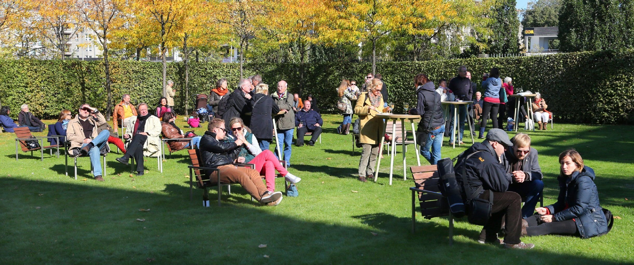 Menschen sitzen bei strahlendem Sonnenschein im Garten der Landesvertretung des Saarlandes in Berlin und genießen den Tag der offenen Tür der Landesvertretungen in den Ministergärten.