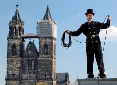 Nahe dem Magdeburger Dom steht der Schornsteinfegergeselle Gunnar Ebeling auf einem Dach in der Innenstadt und reinigt einen Schornstein. (Foto: dpa)