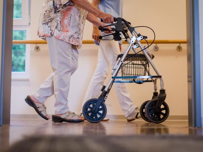 Eine Pflegekraft geht mit einer älteren Frau über einen Korridor in einem Pflegeheim. Der Mindestlohn für mehr als eine Million Pflegekräfte in Deutschland wird erhöht. Foto: Christoph Schmidt/dpa