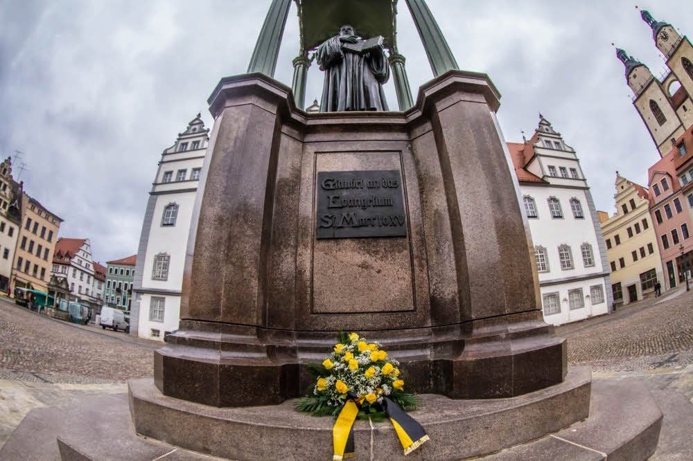Die Augenbinde (kleines Foto) war am Montag schnell wieder weg vom Luther-Denkmal in Wittenberg. Am Dienstag folgten die Blumen: Martin Luther wurde am 10. November 1483 in Eisleben geboren.