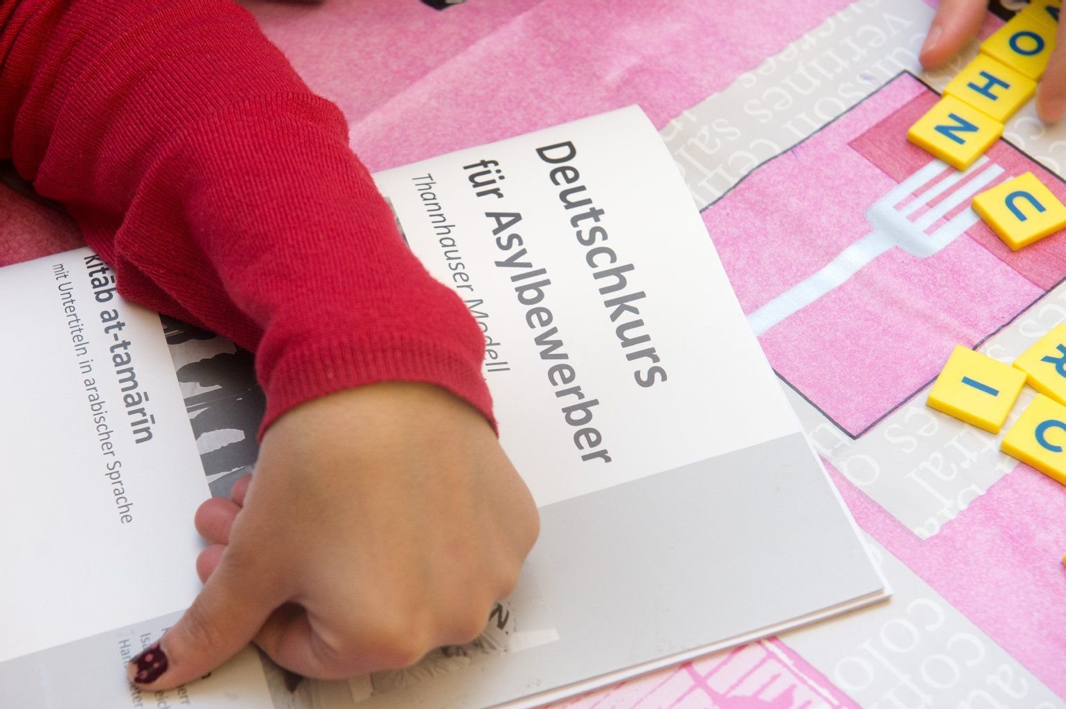 Auf einem Arbeitsheft "Deutschkurs für Asylbewerber" liegt eine Hand bei einem Deutschkurs für Flüchtlinge