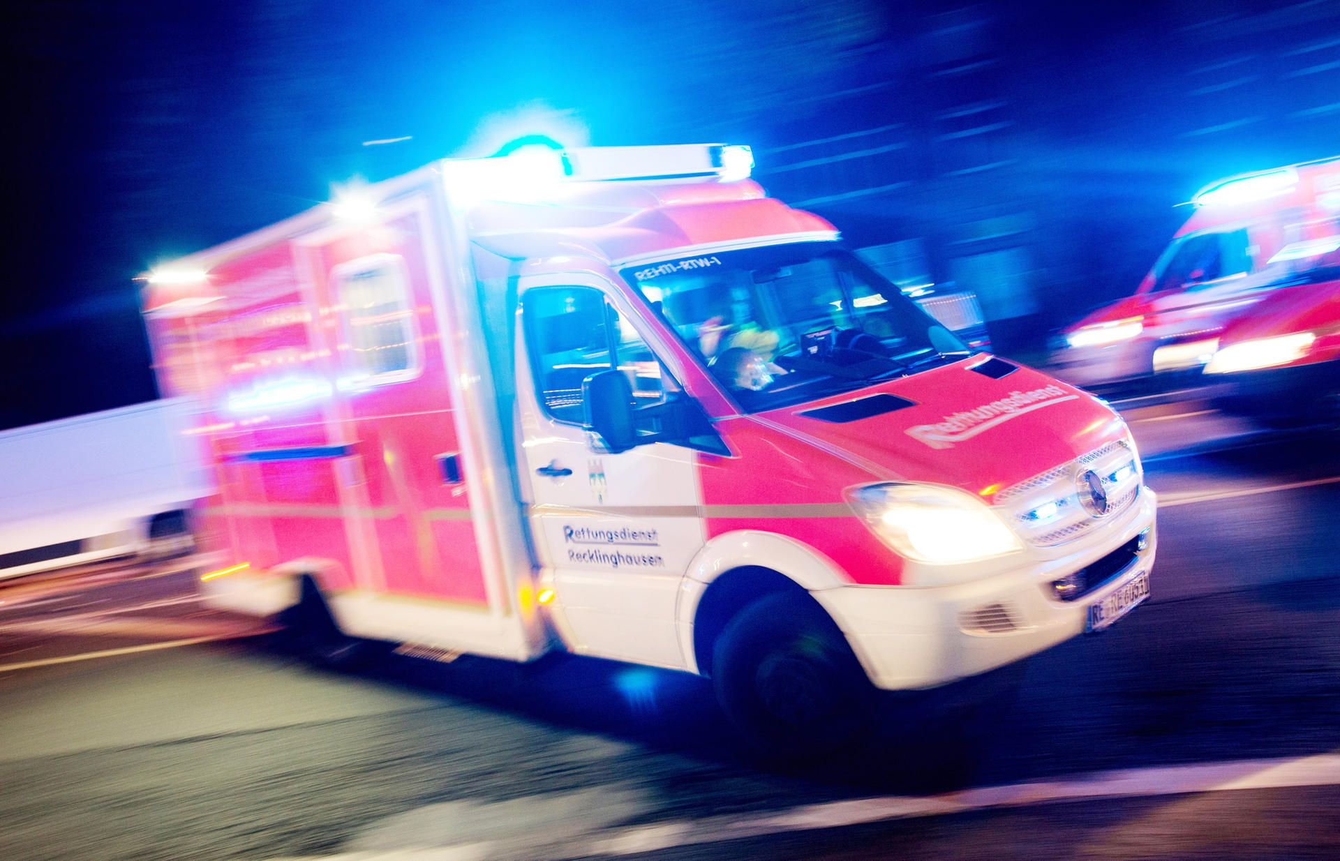 Ein Rettungswagen der Feuerwehr fährt im Dunkeln mit Blaulicht durch eine Straße.