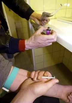 Die nachgestellte Aufnahme zeigt zwei Drogensüchtige, die Heroin spritzen, bzw. auf einem Stück Alufolie mittels eines Feuerzeuges zum Rauchen vorbereiten. (Foto: dpa)