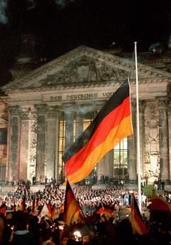Das Archivfoto vom 03.10.1990 zeigt die Einheitsfeier vor dem Berliner Reichstagsgebäude, wo junge Sportler um Mitternacht (02.10. auf den 03.10.1990) vor einer jubelnden Menschenmenge die deutsche Flagge hissen. (Foto: dpa)