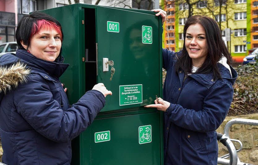 Andrea Bechtel (l., Klimaschutzmanagerin der Stadt) und Patricia Jentsch (Tourist-Information) an der E-Bike-Ladestation auf dem Markt in Merseburg. Den Schlüssel dazu gibt es in der Stadtinfo.
