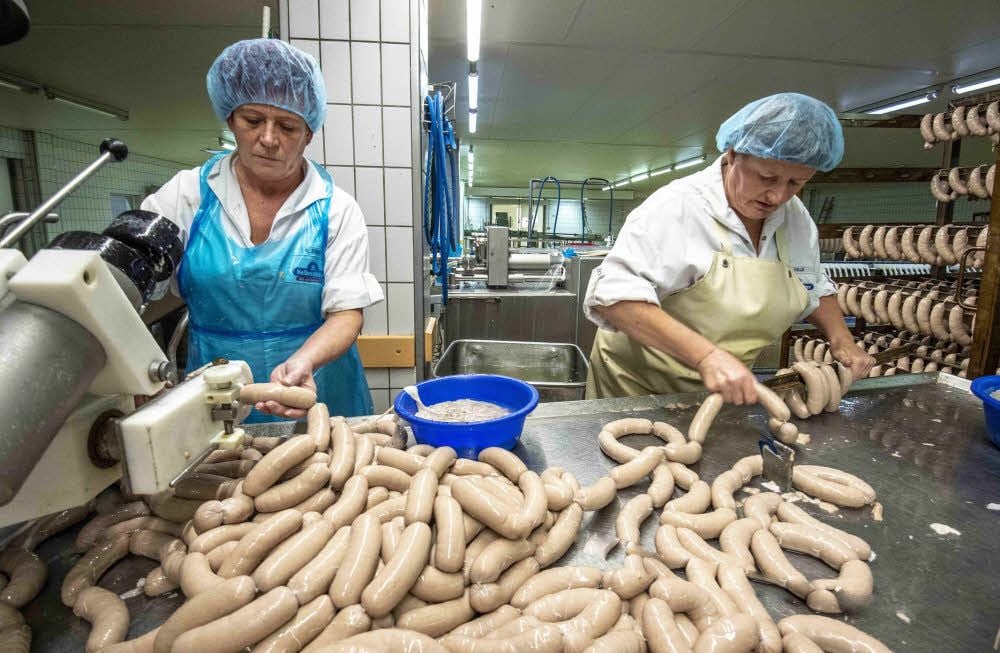 Kerstin Ebing füllt die Wurstmasse in den Darm und Gudrun Hille (rechts) gibt die Würste in ein Gestell zur Weiterverarbeitung.