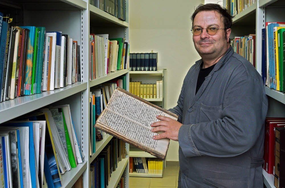 Ralf Schade hält das älteste Stück - ein Protokollbuch aus Rössen aus dem Jahr 1715 - in den Händen.
