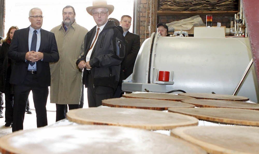 Tischlermeister Rainer Böhme mit seinem aus Holz gefertigten Hut im Gespräch mit Matthias Zscheile (links) von der Hochschule Rosenheim und Jürgen Rogahn, Hauptgeschäftsführer der Handwerkskammer Halle. Im Vordergrund sieht man die Baumscheiben nach der Bearbeitung.