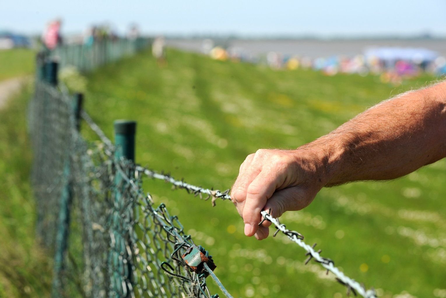 Ein Nordseetourist prüft den Stacheldrahtzaun am Strand von Hooksiel (Niedersachsen).