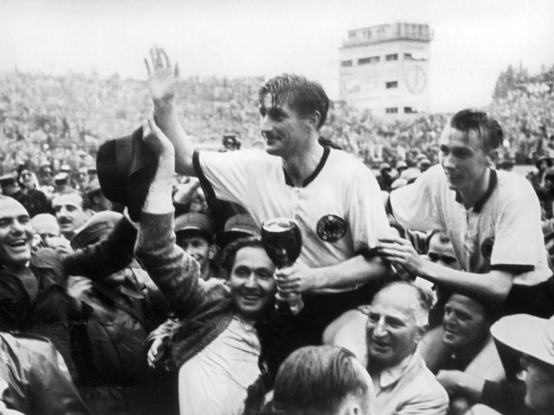 Der deutsche Stürmer und Kapitän Fritz Walter (M, oben) und sein Lauterer Teamgefährte Horst Eckel (r) werden nach dem Triumph im Fußball-WM-Finale im Berner Wankdorfstadion von begeisterten Anhängern vom Spielfeld getragen. Foto: picture alliance/dpa/Archivbild