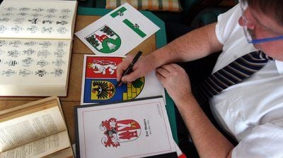 Der Heraldiker Jörg Mantzsch sitzt in seinem Haus in Magdeburg zeichnend an einem Tisch. (FOTO: DPA)