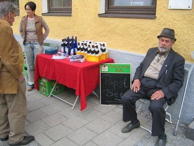 In einer Szene des Dokumentarfilms «Wir sind Papst! - Marktl am Inn» sitzt ein Bewohner neben einem Stand mit Papst-Bier in Marktl am Inn. (FOTO: DPA)