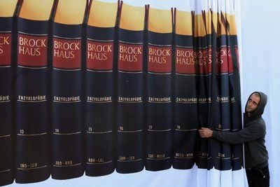 Einen mit Brockhaus-Bänden bedruckten Vorhang justiert ein Messe-Arbeiter auf der Buchmesse in Frankfurt am Main. (ARCHIVFOTO: DPA)
