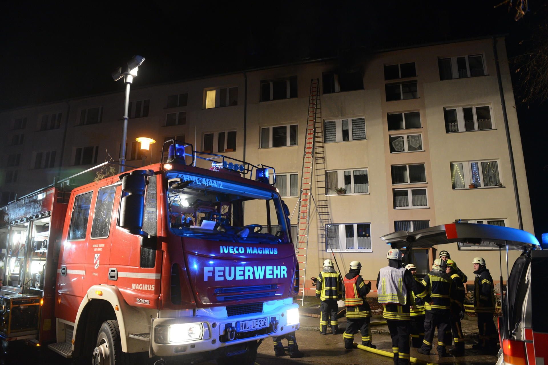 Feuerwehrleute stehen in Premnitz vor einem Wohnhaus in dem eine Wohnung gebrannt hat.