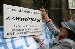 Eine Frau befestigt auf der 19. Mahnwache für die im Irak entführten deutschen Ingenieure am Montag (3. April 2006) an der Leipziger Nikolaikirche ein Schild mit der Internetadresse «www.wehope.de». (Foto: dpa)