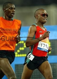 Der blinde Läufer Henry Wanyoike (r) aus Kenia ist bei den Paralympics in Athen im 10.000-Meter-Lauf auf dem Weg zur Goldmedaille.Er wird von einem Begleitläufer geführt (Archivfoto vom 19.09.2004). Der 31-Jährige ist vor zehn Jahren plötzlich erblindet. Seitdem hat er über 5000 und 10.000 Meter mehrere Goldmedaillen bei den Paralympics gewonnen. Inzwischen läuft er Marathon. Blinde haben es schwer in Kenia - oft werden sie von ihrer Familie ausgestoßen. (Foto: dpa)