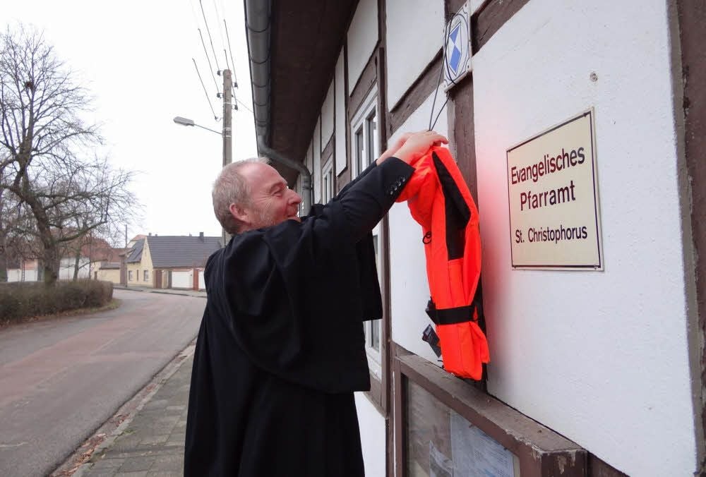 Pfarrer Ronald Höpner befestigt eine Rettungsweste am Pfarrhaus in Quellendorf. Wenn man darüber redet, würde ihn das freuen.