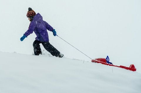 Ein Mädchen zieht ihren Bob auf einen schneebedeckten Berg. (FOTO: DPA)