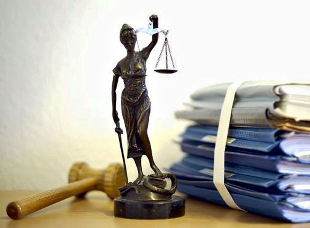 Die Statue einer Justizia steht neben einem Stapel Akten.