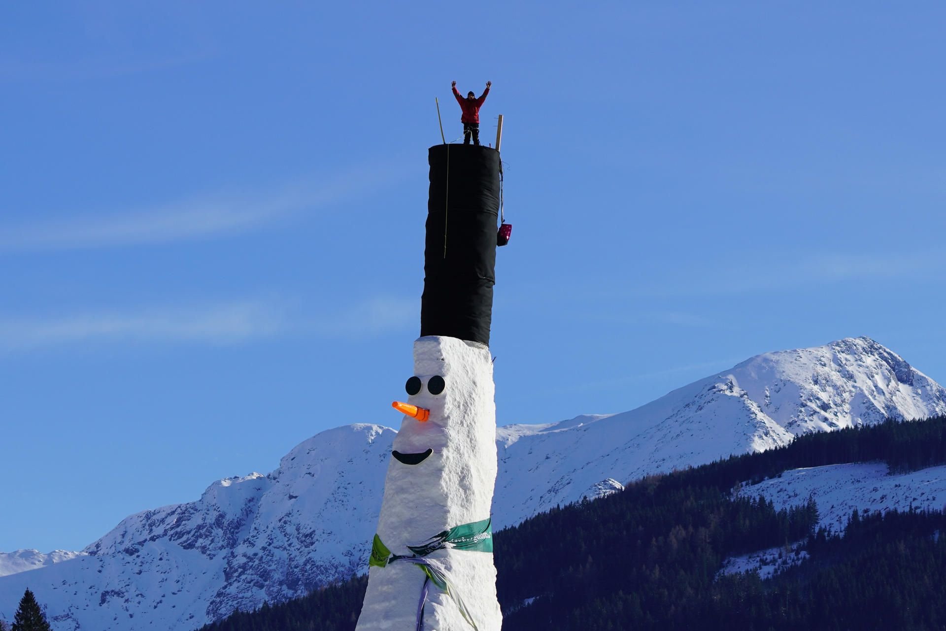 Ein Mann steht in Donnersbachwald (Österreich) auf dem Zylinder auf einem Schneemann.