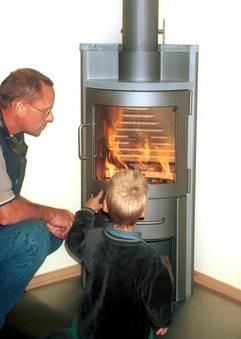 Das Archivbild vom 20.12.2000 zeigt einen Vater, der zusammen mit seinem Sohn das Feuer in einem Kaminofen in einer Münchner Wohnung betrachtet. Knisternde Flammen, wohlige Wärme und tanzende Schatten an den Wänden: Immer mehr Deutsche verbinden Romantik mit einer guten Öko-Bilanz und lassen sich Kamine und Kachelöfen in ihre Häuser einbauen. (Foto: dpa)