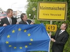 Der rheinland-pfälzische Ministerpräsident Kurt Beck (2.v.r.) entfaltet am Ortsschild des Westerwalddorfes Kleinmaischeid gemeinsam mit Bürgermeister Horst Rasbach (l.) und Landrat Rainer Kaul (r.) eine Europaflagge. (Foto: dpa)