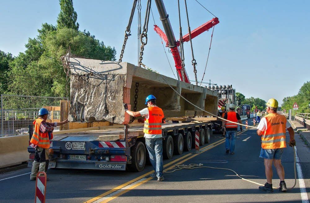 Maßarbeit - mit Hilfe von Kran und Halteseilen wird das 60 Tonnen schwere Brückenteil auf einen Schwerlasttransporter gehievt.
