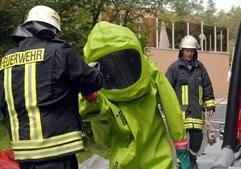 Ein Feuerwehrmann hilft seinem Kollegen am Mittwoch (11.07.2007) aus einem Schutzanzug, nachdem dieser von der Unfallstelle mit Chlor im Centerpark Gunderath (Kreis Vulkaneifel) zurückgekehrt ist. (Foto: dpa)