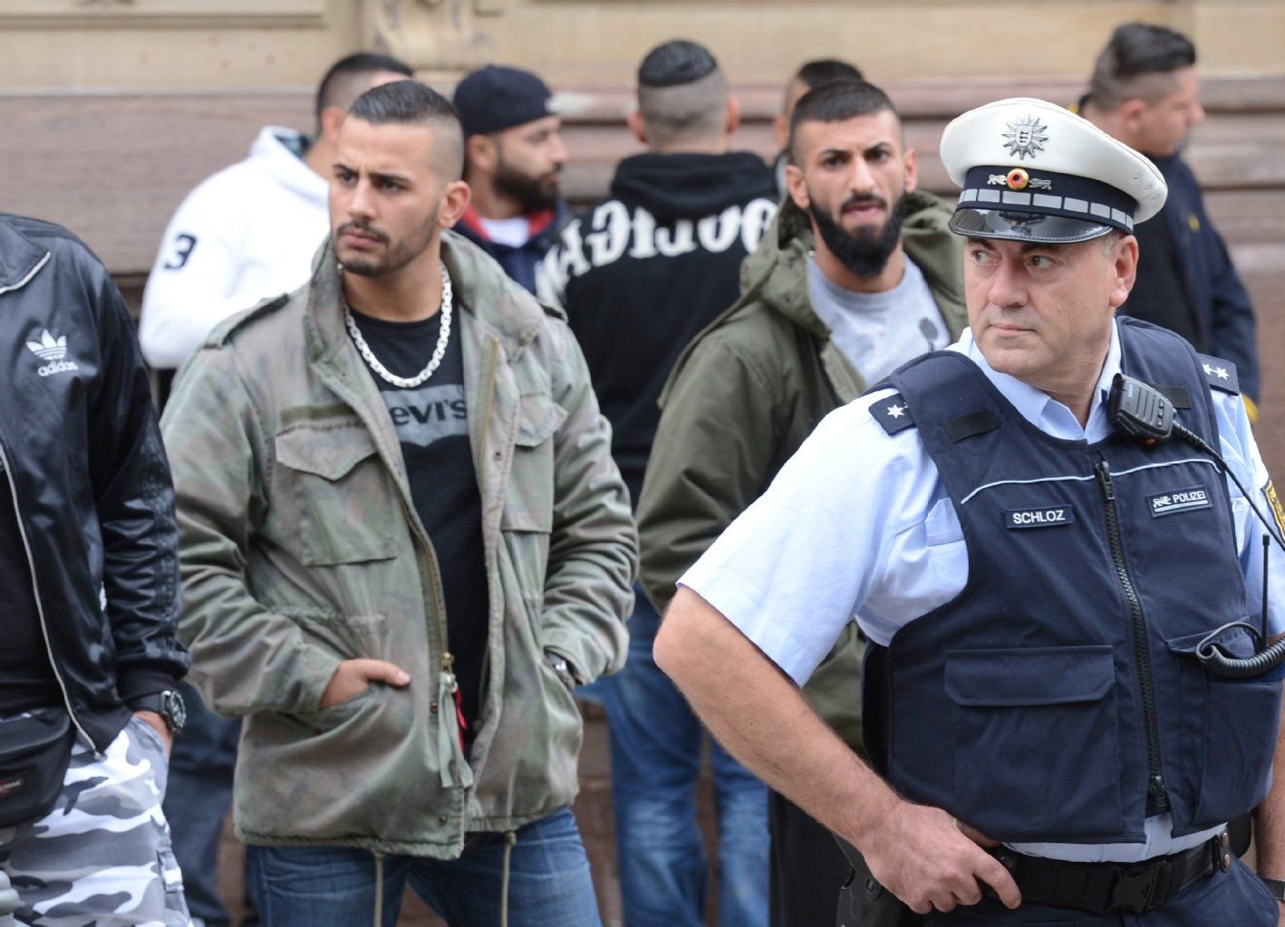 Ein Polizist steht vor Anhängern der Rockergruppe Red Legions vor dem Landgericht in Stuttgart. Bei einem Bandenkrieg zwischen den Rockergruppen Red Legions und Black Jackets in Esslingen wurde 2012 ein Mann getötet. Elf Angeklagten wird nun gemeinschaftlicher Mord vorgeworfen.