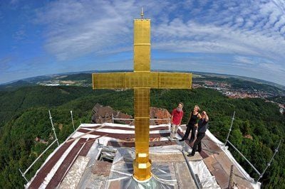 Das drei Meter hohe, neu vergoldete Kreuz auf dem Bergfried der Wartburg wird von Steinmetz Meinhart Vierkant, der Leiterin der Bauhütte Annette Felsberg und Diplomrestaurator Stephan Scheidemann (v.l.) betrachtet. (FOTO: DPA)