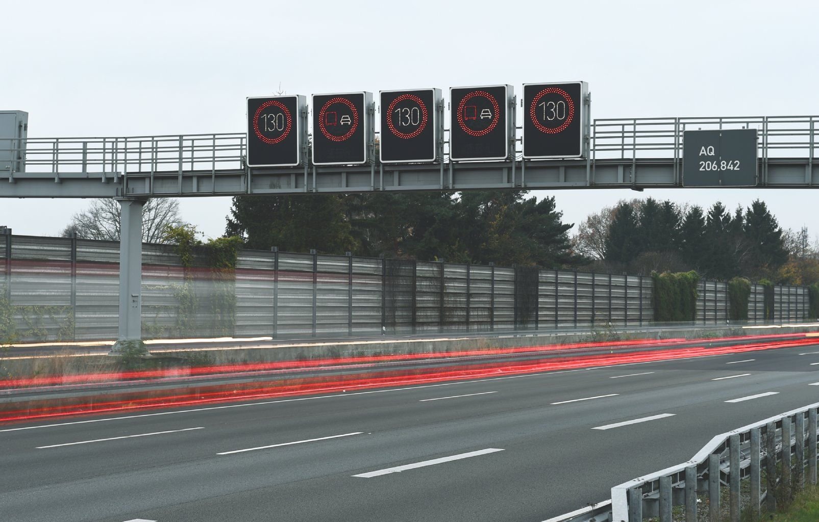 Der Verkehr fließt auf einer Autobahn unter einer Schilderbrücke hindurch.
