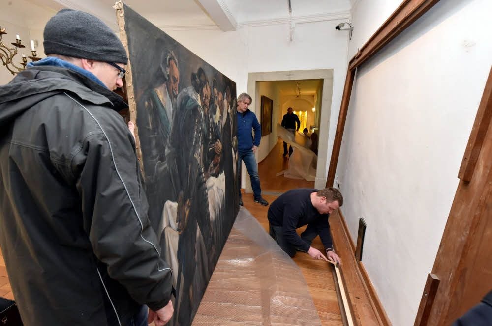 Diplomrestaurator Mirko Negwer (r.) bereitet den Rahmen vor. In diesen soll das restaurierte Bild von Gustav Adolfs Obduktion, das von zwei Helfern gehalten wird, wieder eingehängt werden.