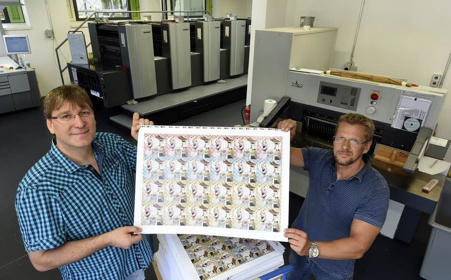 Druckerei-Chef Frank Robrecht und sein Kollege Frank Just halten den ersten Bogen, den die neue Druckmaschine der Kunsthochschule ausgeworfen hat.