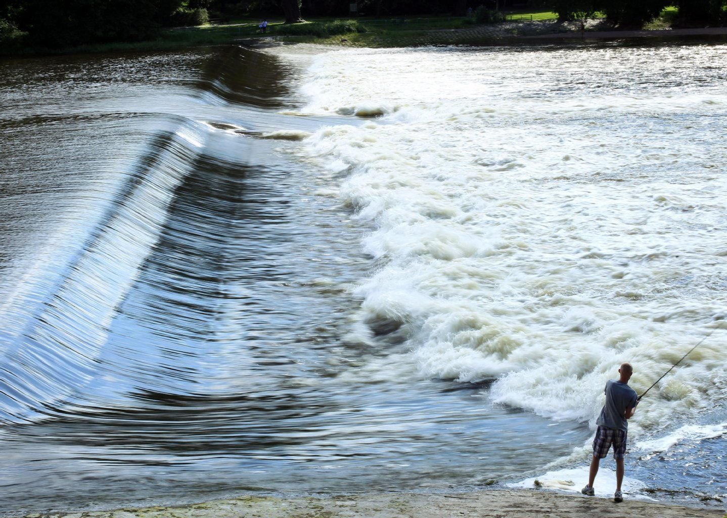 Ein Angler fischt am Wasserfall in der Alten Elbe in Magdeburg.