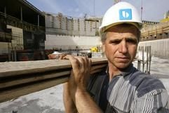 Ein Bauarbeiter trägt auf einer Baustelle Bretter. (Foto: dpa)