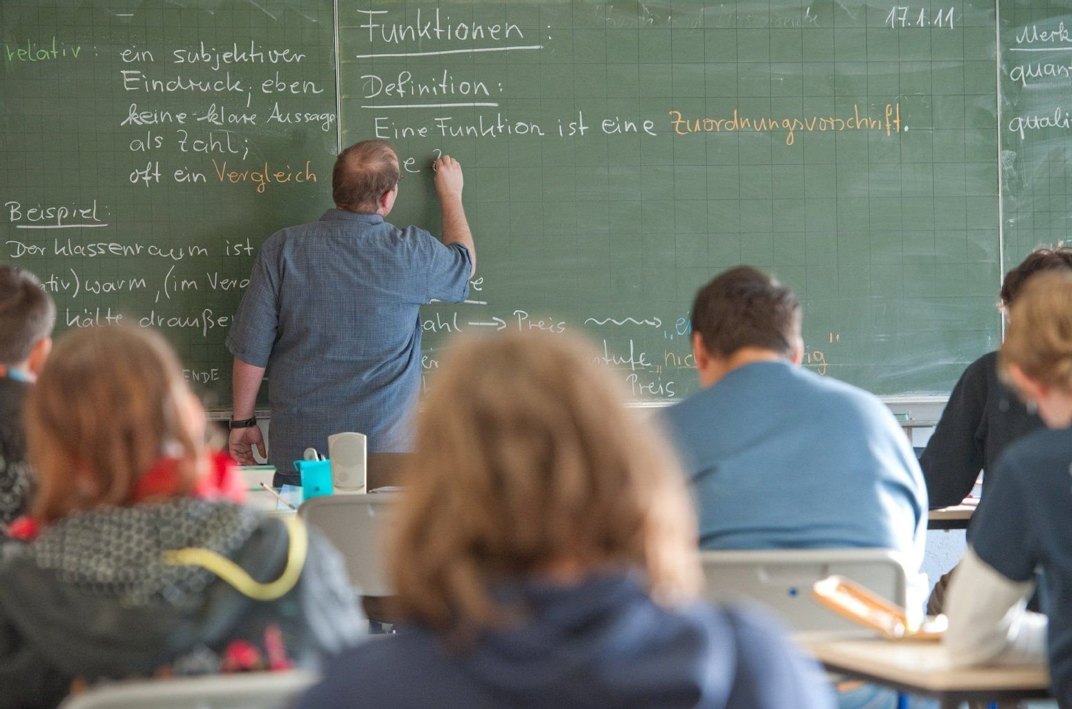 Ein Lehrer schreibt während einer Schulstunde an die Tafel.